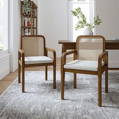 two chairs sitting on top of a rug in front of a table with a vase