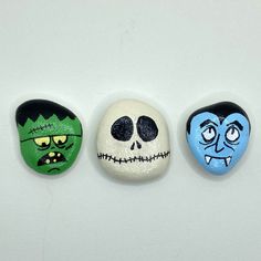 three rocks with faces painted on them are lined up in a row against a white background