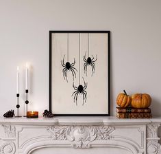 a mantel with candles, pumpkins and a spider print on the wall above it