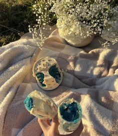 someone is holding their hand up to some cupcakes on a blanket with flowers in the background