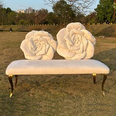 a bench with two white roses on it in the grass near some trees and buildings