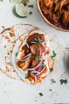 two tacos with meat, onions and cilantro on them next to a bowl of salsa