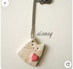 a white ceramic cat with a pink heart on it's face is attached to a silver chain