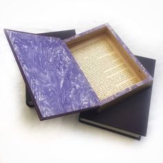 an open book sitting on top of two black books with purple paper in the middle