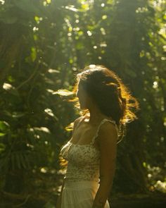 a woman in a white dress is walking through the woods with her hair blowing in the wind