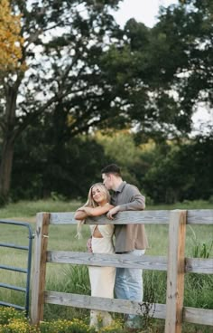 a man and woman standing next to each other near a wooden fence in the grass