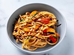 a bowl filled with pasta and vegetables on top of a white countertop next to a fork