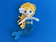 a crocheted mermaid doll with blonde hair and blue dress sitting on a blue background