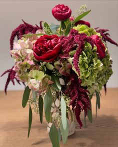 a vase filled with red and green flowers on top of a wooden table in front of a white wall