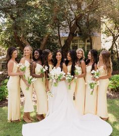 a group of women standing next to each other in front of trees and grass with bouquets