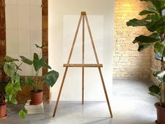 a wooden easel next to potted plants in front of a brick wall