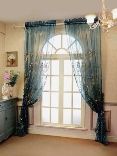 a room with a large window covered in blue drapes and flowers on the curtains