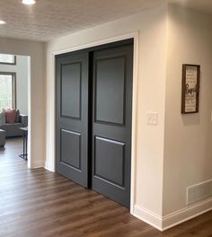 an empty living room with two doors and hard wood flooring in the middle of it