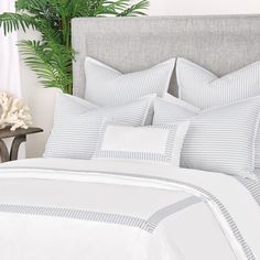 a bed with white and grey striped comforter next to a potted palm tree