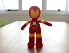 a crocheted iron man sitting on top of a wooden table next to a window