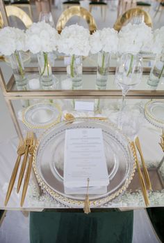 the table is set with white flowers and gold place settings