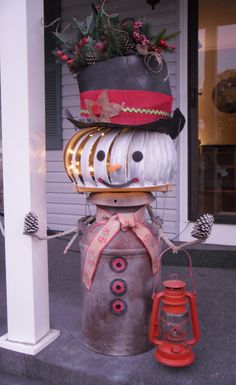 a snowman with a top hat and scarf on it's head sitting in front of a house