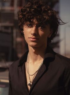 a young man with curly hair wearing a black shirt and some necklaces on his neck