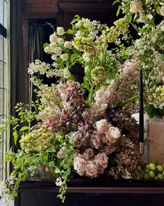 an arrangement of flowers and greenery in front of a window