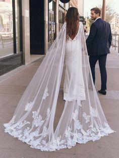 a bride and groom walking down the street in front of a building wearing veils