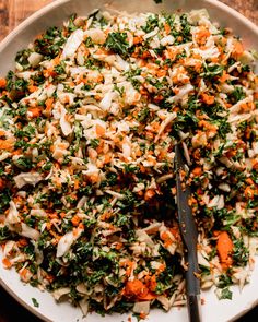 a white bowl filled with carrots, cabbage and parsley on top of a wooden table