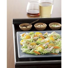 a salad with dressing on a tray next to two glasses of wine and chopsticks