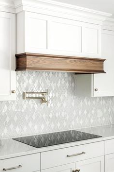 a kitchen with white cabinets and marble backsplash, wood hood over the stove