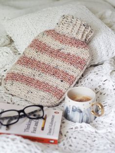 a knitted mitt, coffee cup and book on a bed with eyeglasses