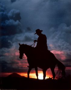 a man riding on the back of a horse under a cloudy sky at sunset or dawn