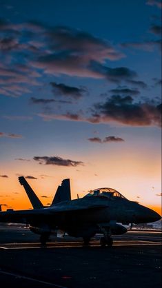 a fighter jet sitting on top of an airport tarmac at sunset with clouds in the background