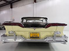 the back end of an old car in a garage with other classic cars behind it