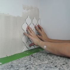 a woman is painting a wall with white paint and green tape on the floor next to it