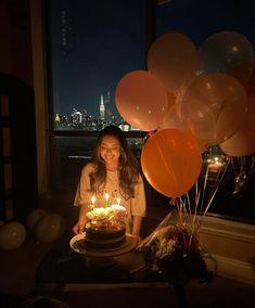 a woman sitting in front of a birthday cake with candles on it and balloons around her