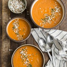 three bowls filled with carrot soup on top of a wooden table