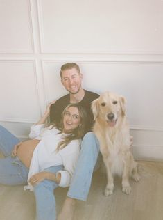 a man and woman sitting on the floor next to a brown dog with their arms around each other