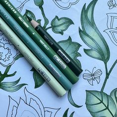 three green pencils sitting on top of a flowered sheet