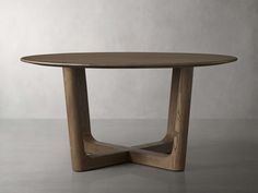 a round wooden table sitting on top of a cement floor next to a white wall