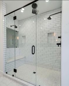 a walk in shower sitting next to a white tiled wall and floor with black accents