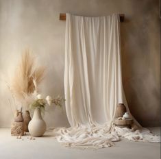 three vases with flowers in front of a white drapeed curtain and some feathers on the floor