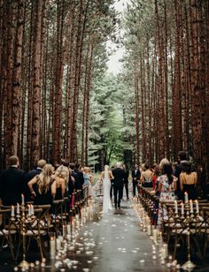 a wedding ceremony in the woods with candles on the aisle and people walking down the aisle