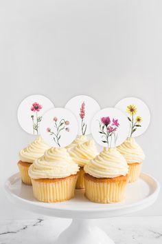 three cupcakes with white frosting and flowers on them sitting on a cake plate