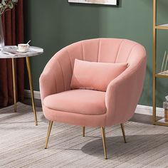 a pink chair sitting on top of a wooden floor next to a table with a vase