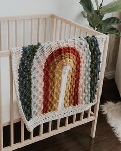 a crocheted blanket hanging from the side of a crib next to a potted plant