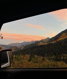 the view from inside a car looking at mountains and trees in the distance with a sunset