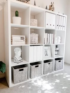 a white book shelf filled with lots of books and wicker baskets next to a potted plant