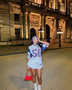 a woman standing on the street in front of an old building at night wearing a football jersey