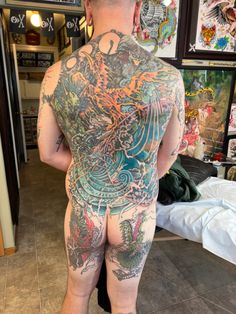 a man with tattoos on his back standing in front of a mirror