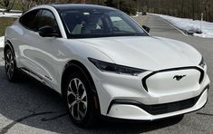 a white electric car parked in a parking lot with snow on the ground and trees behind it