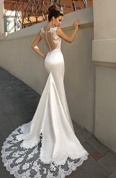 a woman in a white wedding dress is standing on a ledge with her back to the camera