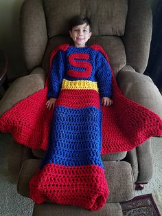 a young boy in a superman costume is laying on a reclining chair with a crocheted blanket